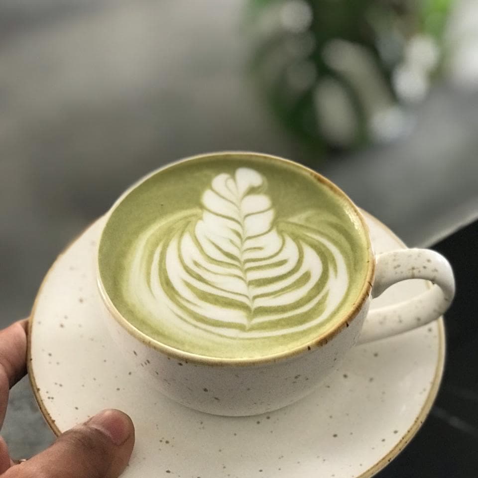 Latte art berbentuk rosetta dalam cangkir di Relung Kopi